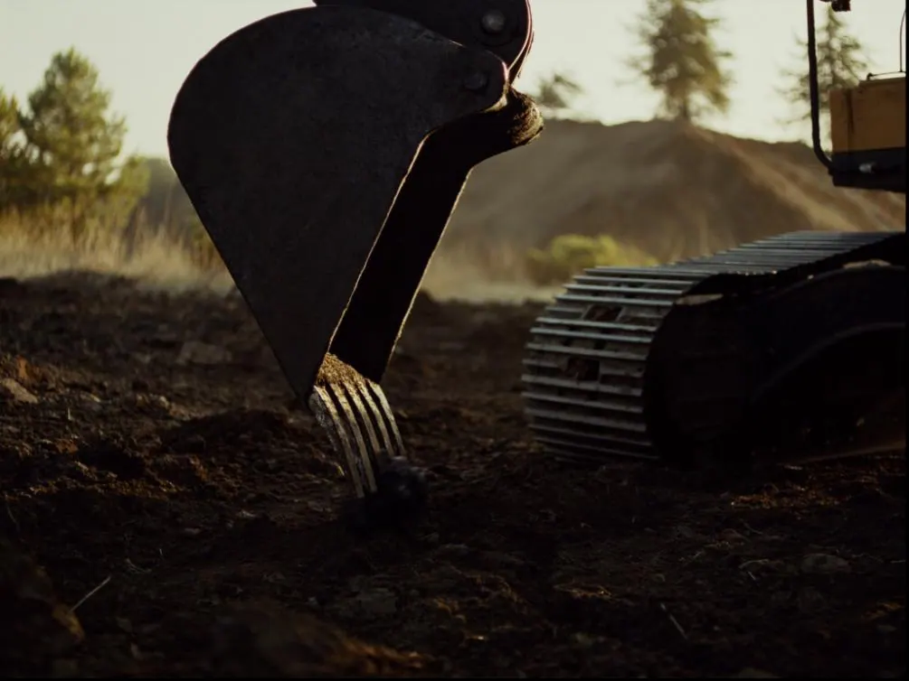 Close view of an excavator bucket and worn steel teeth resting on freshly turned earth.