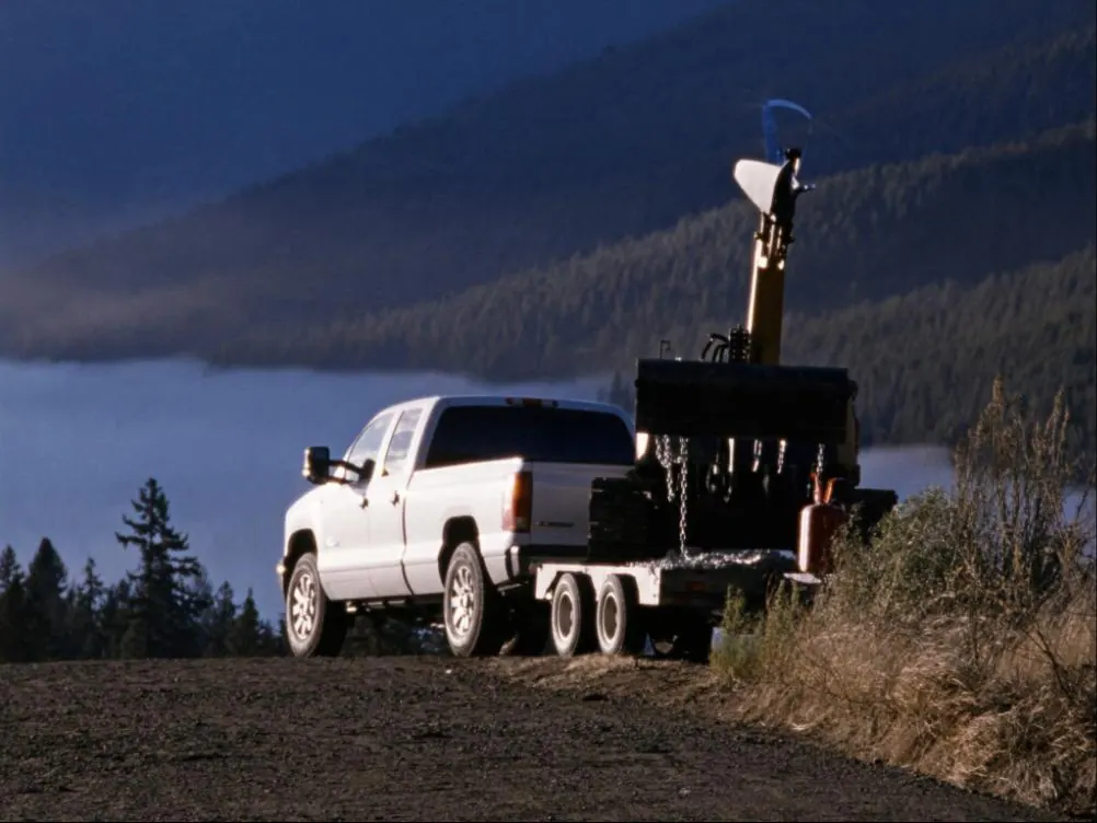 A work truck and equipment trailer loaded with an excavator, parked at a rural jobsite at first light.
