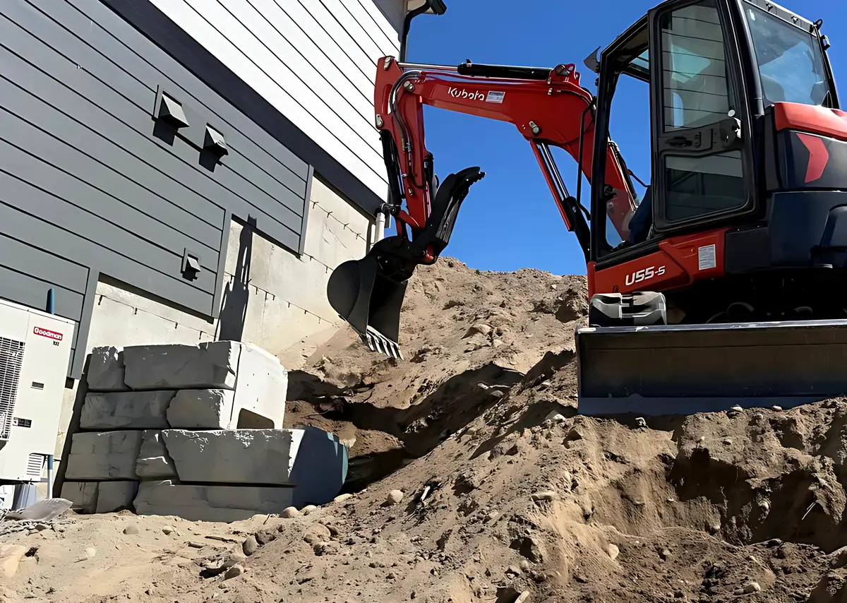 Kubota U55-5 digging beside a house next to a stacked concrete block wall