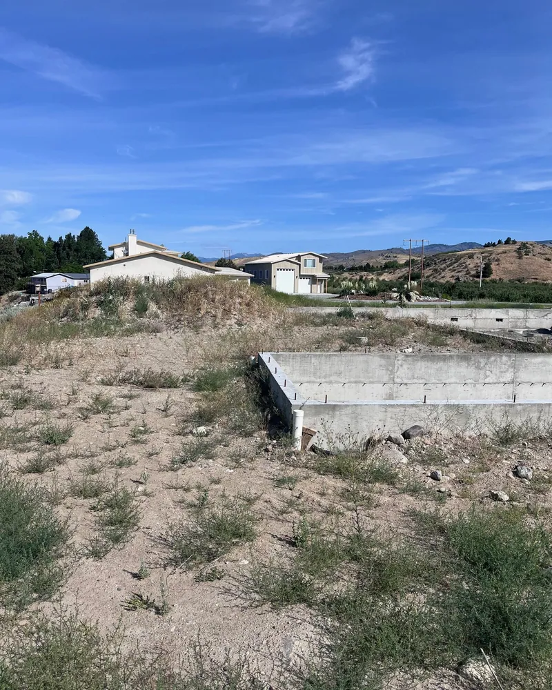 The lot from the other end, weeds growing through the concrete foundation walls
