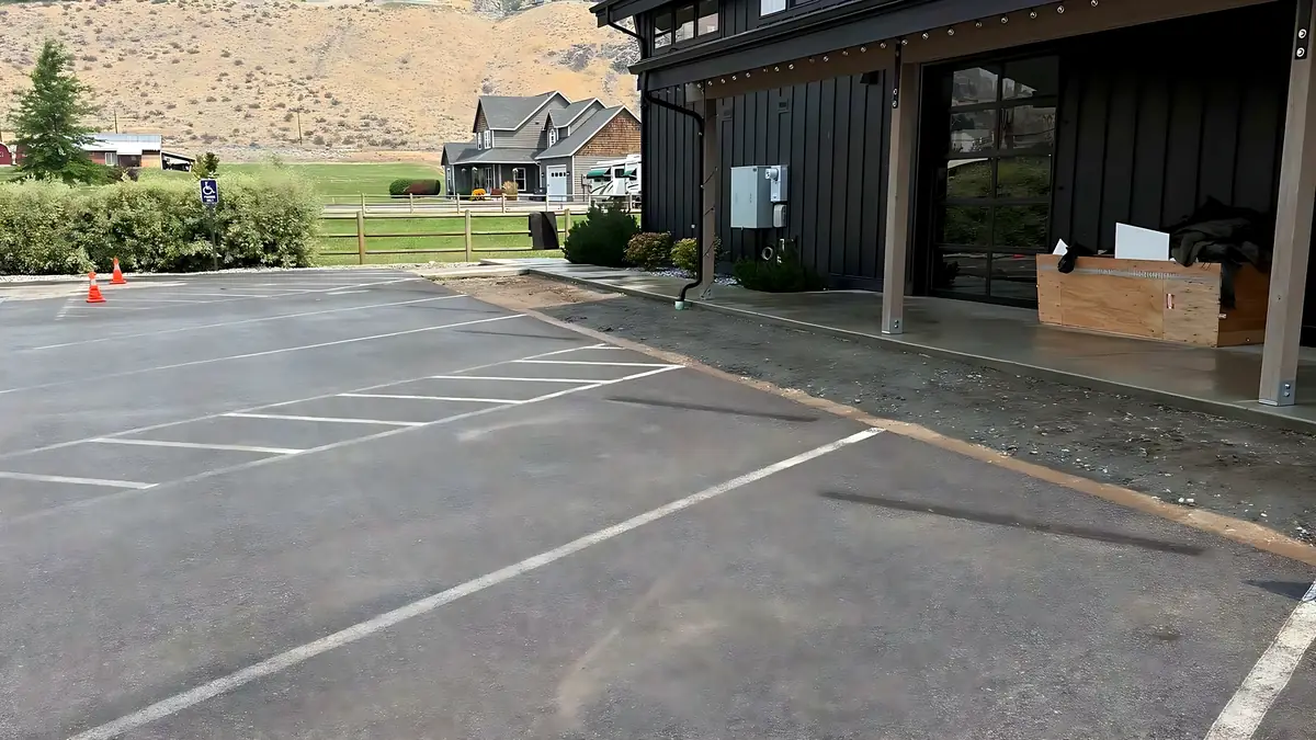 Paved and striped parking lot beside a dark commercial building with dry hills behind